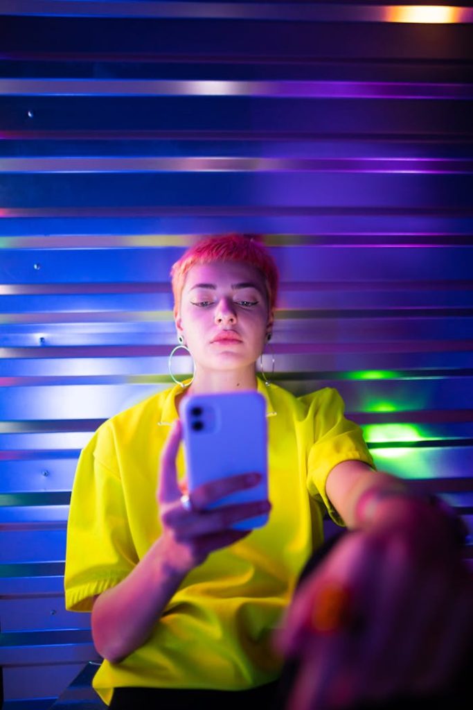 a-short-haired-woman-in-yellow-shirt-using-a-mobile-phone-8941771 A young woman in a yellow shirt uses her smartphone, bathed in vibrant neon lighting.